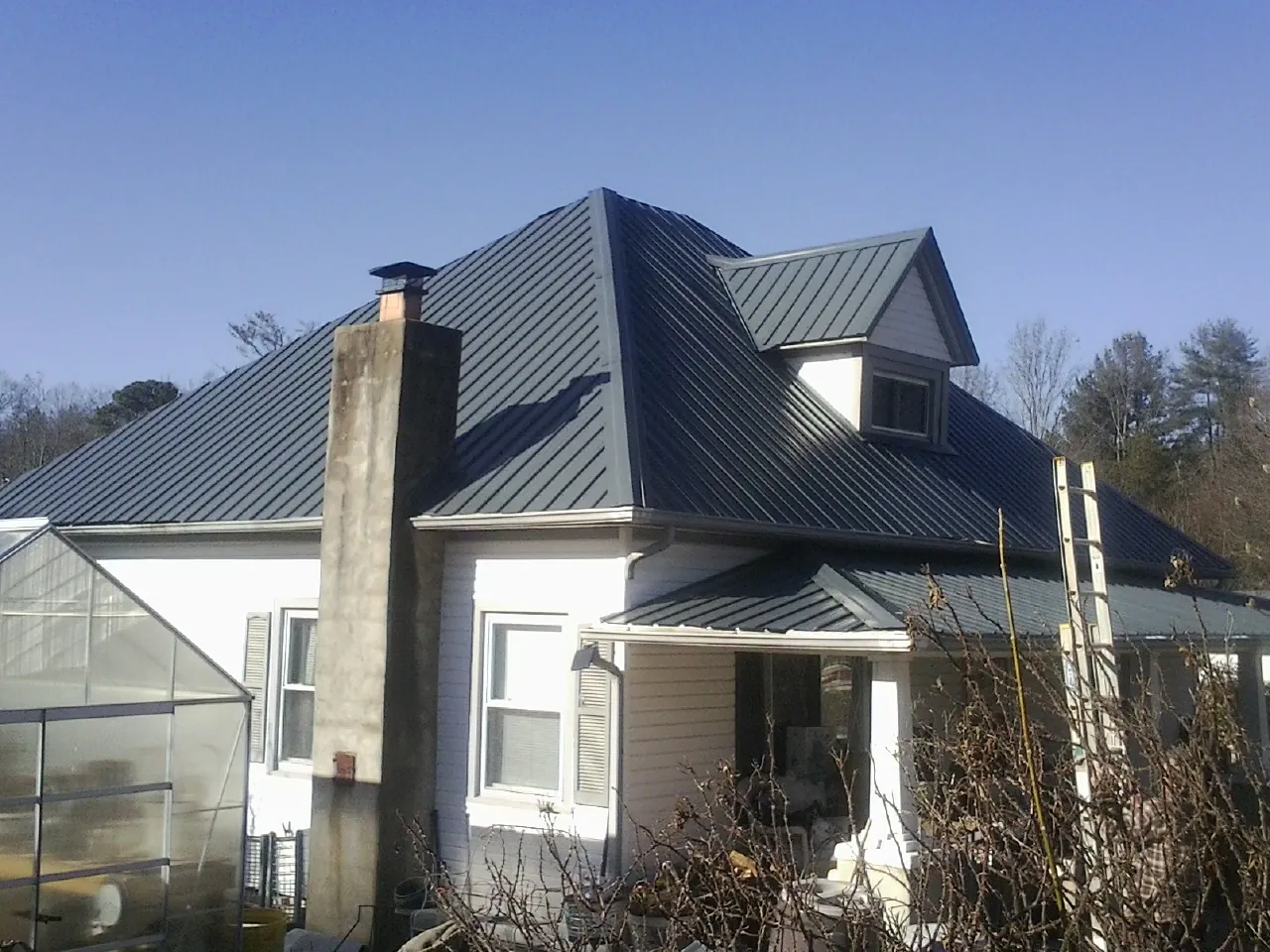 Dark blue standing seam metal roof on a white farmhouse with dormer — Slate & Tile Roof Repair by Roofing Brothers in Jesup
