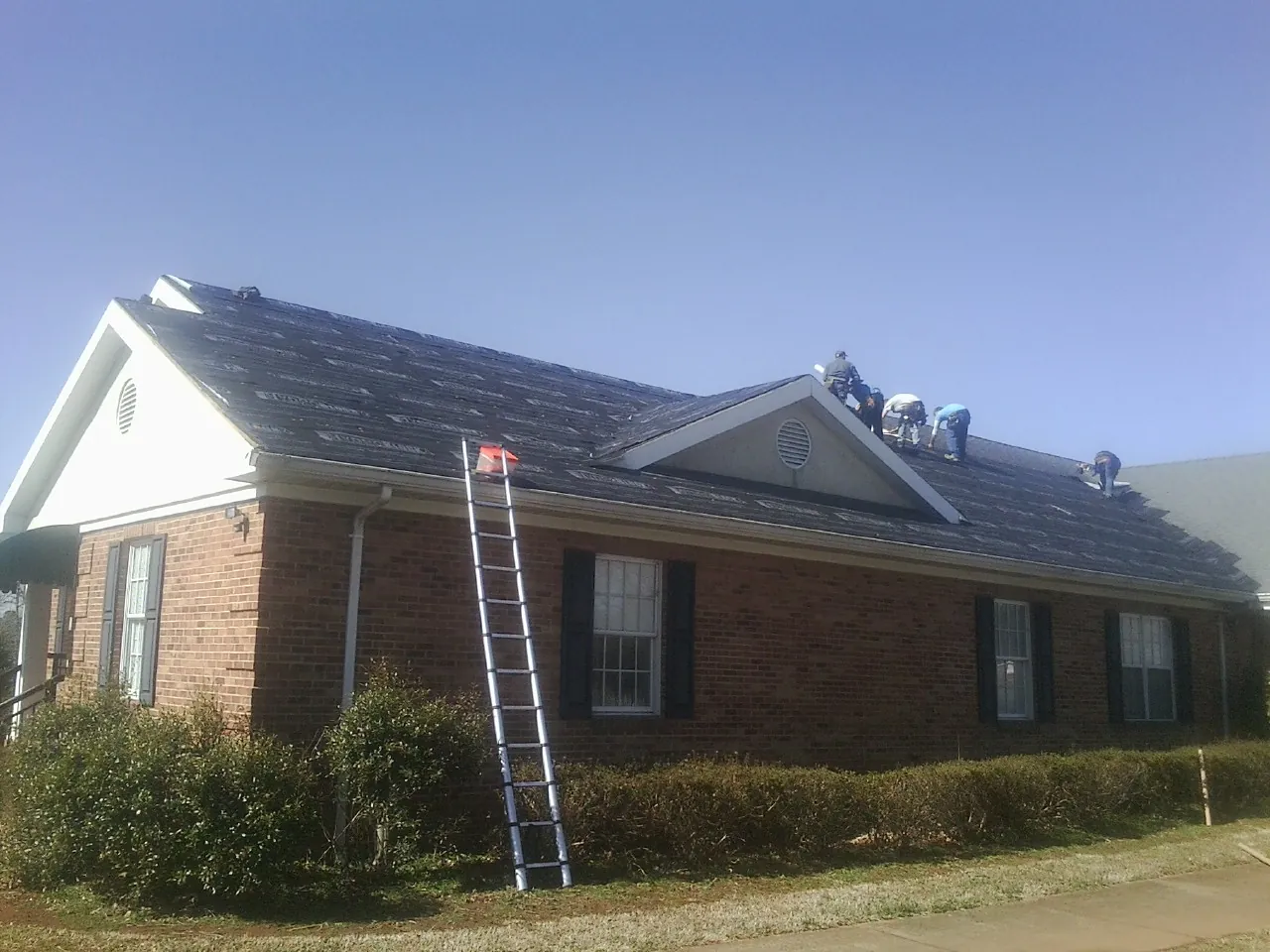 Crew tearing shingles off a brick ranch roof with a ladder set — Emergency Roof Repair work by our crew in Jesup