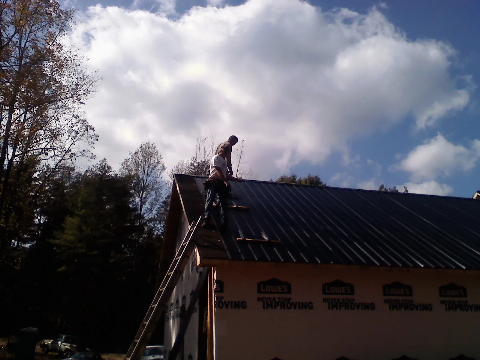 Roofer fastening dark metal panels high against a cloudy sky, from a Roof Inspection job in Jesup