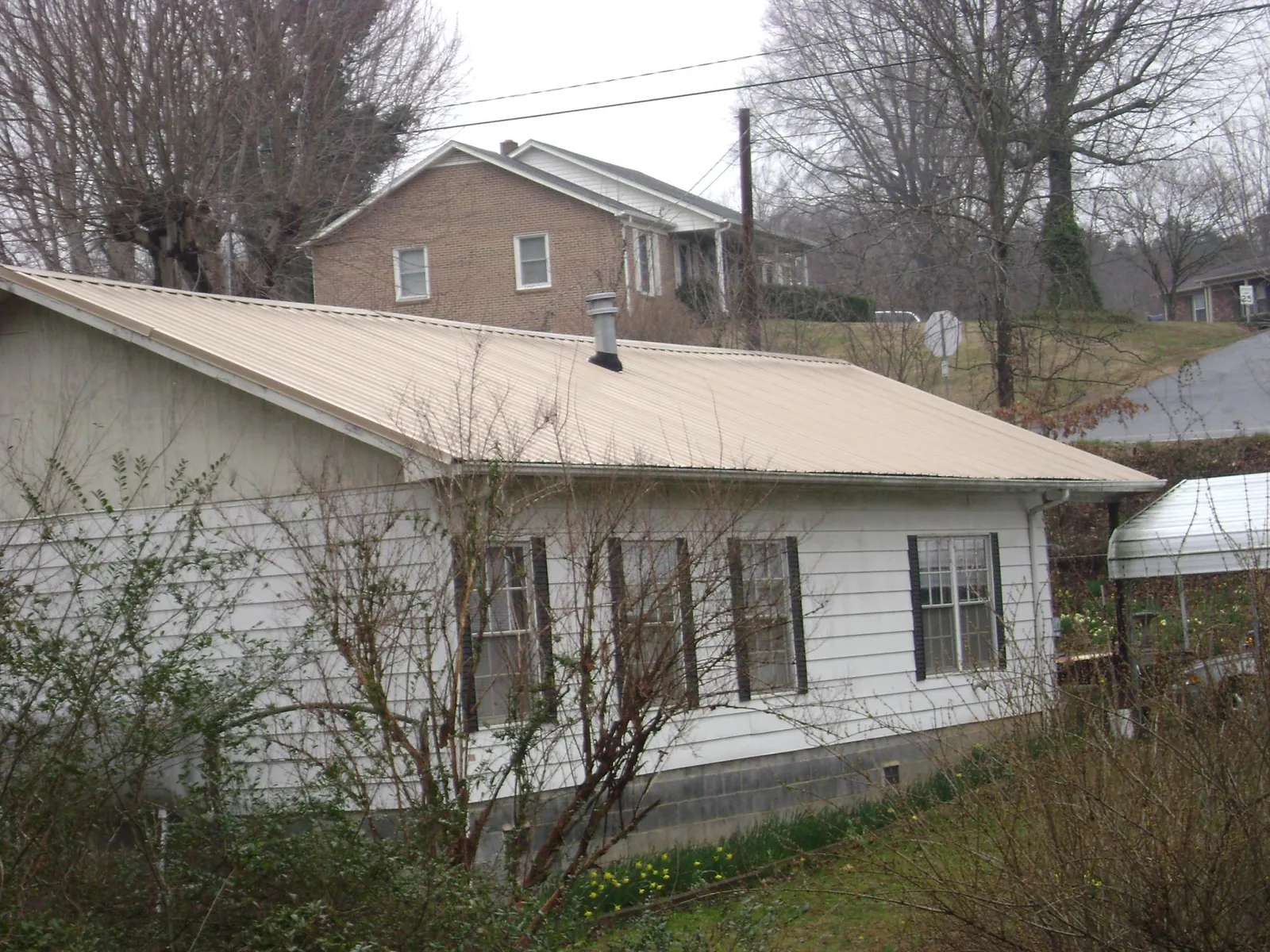 Tan metal roof on a white sided house set into a hillside — Commercial Roofing by Roofing Brothers in Jesup